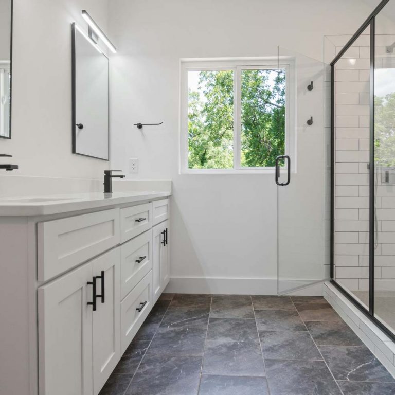 Bright contemporary bathroom with a white double-sink vanity, black faucets, and large mirrors beside a glass-enclosed shower.